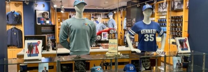 View of the window of the JFK Library Museum store, with books, a sweatshirt, and a tee shirt on display