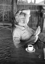 Hemingway reading a newspaper at his camp in Africa, c. 1953.