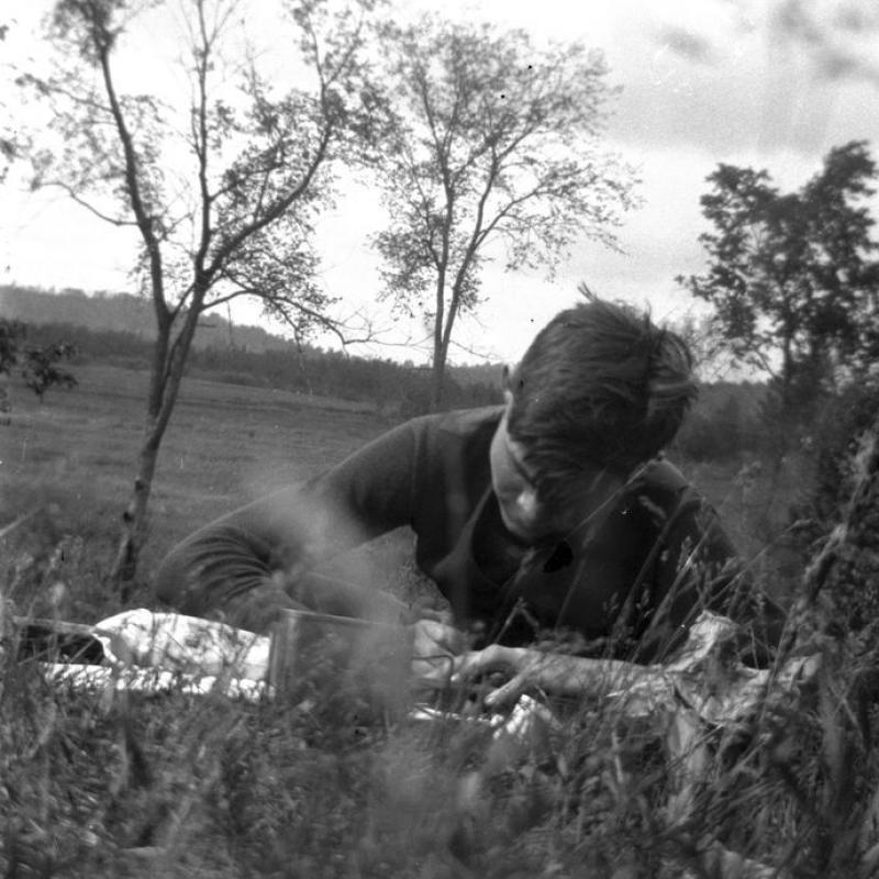 A teenaged Ernest Hemingway lying on his stomach in a field, writing.  Michigan, c. 1914.