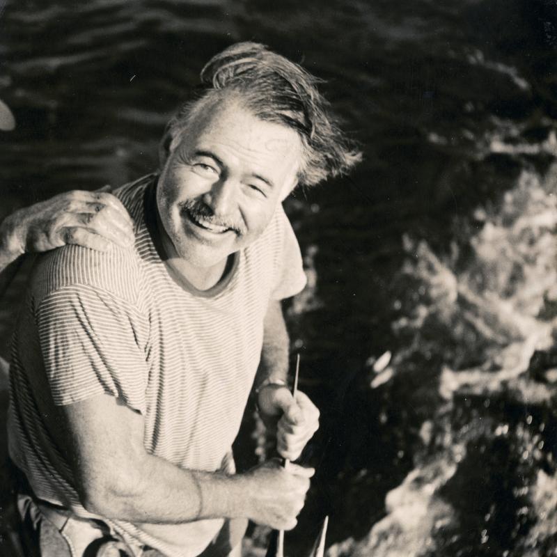 A smiling Ernest Hemingway holds the bill of a marlin on board the PIlar, 1948