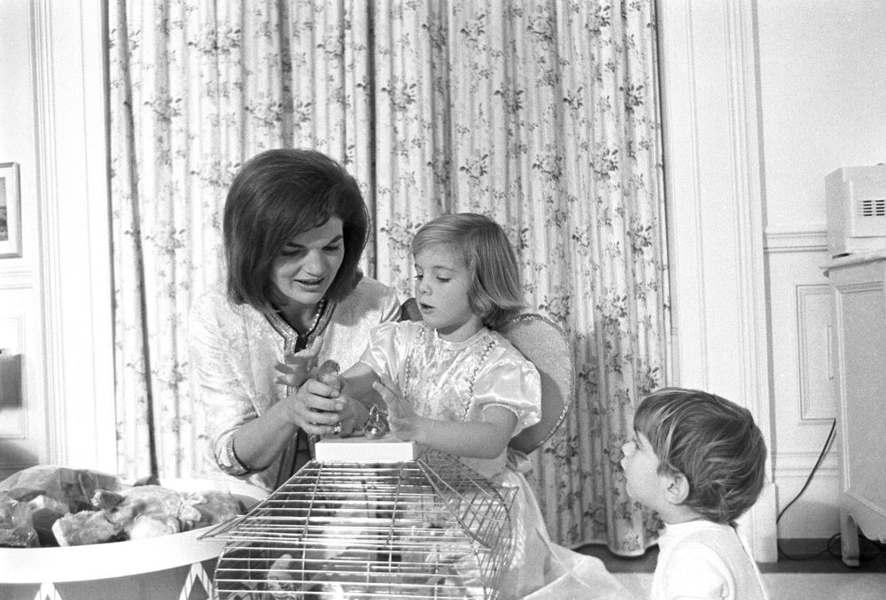 First Lady Jacqueline Kennedy and her children, Caroline and John Jr., visit with parakeets, Bluebell and Maybelle, in John’s nursery, following a joint birthday party for the children.