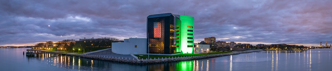 The JFK Library on the water lit up green with an American flag illuminated